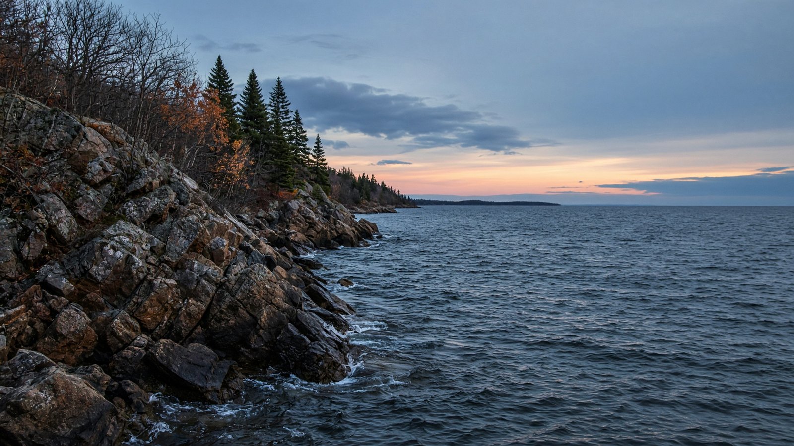 A steep rocky point on a northern lake at dusk in late fall, with bare trees and choppy water.